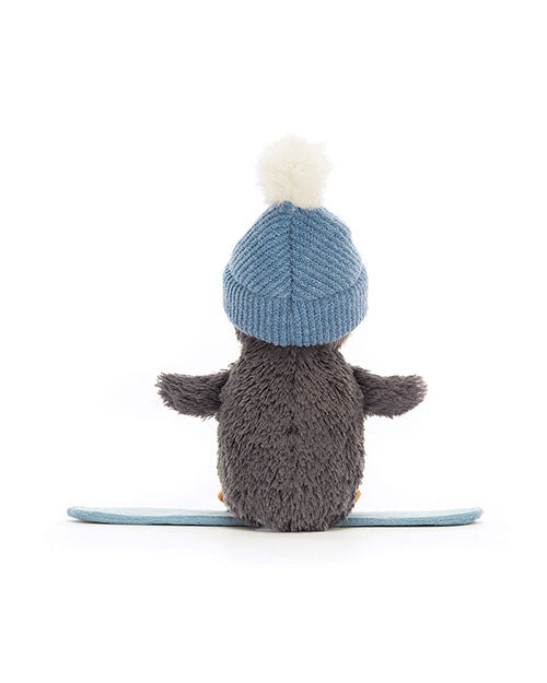 Rear view of a plush penguin toy with outstretched wings, wearing a blue knit hat with a white pom-pom, standing on a light blue surface.