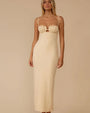 A person wearing a fitted, cream-colored textured dress with a long, straight silhouette that extends to mid-calf. The dress features structured cups with a small cutout detail beneath them and thin shoulder straps tied in small knots at the top. The fabric has a nubby, boucle-like texture throughout.
