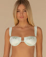 A model wearing a light mint‑green bikini top made of smooth, satin‑finish fabric with a subtle sheen. The design features softly ruched cups with an underwire shape and wide shoulder straps that extend upward from each side