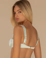 Back view of a model wearing a light mint‑green bikini top made of smooth, satin‑finish fabric with a subtle sheen. The design features softly ruched cups with an underwire shape and wide shoulder straps that extend upward from each side.