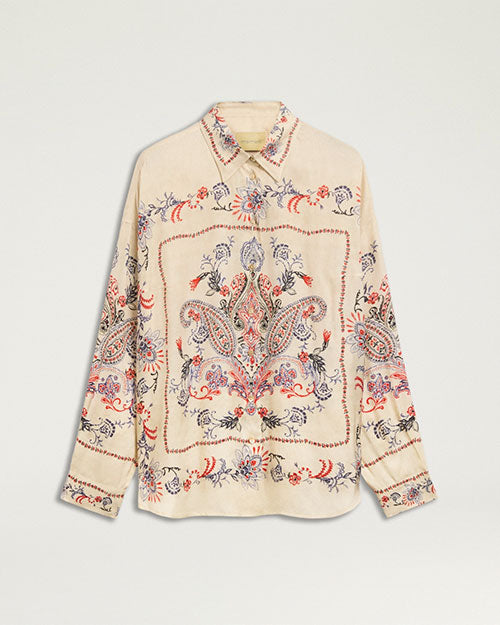Front view of a cream-colored button-front blouse with an intricate paisley print in shades of blue, coral, and red. The long-sleeve blouse features a pointed collar, buttoned cuffs, and a relaxed silhouette. A large ornamental paisley motif is centered on the front, with coordinating border-inspired details across the sleeves and body. Displayed against a light gray background.