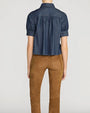 Rear view of a person wearing a dark denim, button down blouse with short puff sleeves and a collar. 