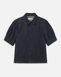 Studio image of a dark denim, button down blouse with short puff sleeves and a collar. 