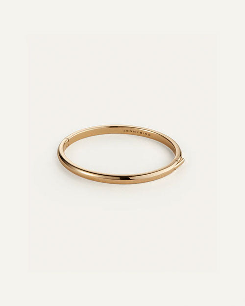 A sleek, polished gold bangle bracelet with a minimalist design and a hinged closure, engraved with the brand name ‘Jenny Bird’ on the inner side.