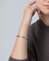 Close-up of a wrist wearing a sleek, polished silver bangle bracelet with a minimalist design, paired with a dark knit top.