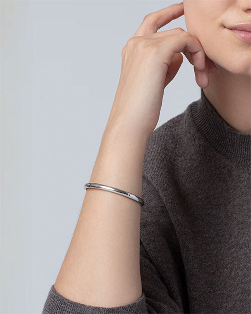 Close-up of a wrist wearing a sleek, polished silver bangle bracelet with a minimalist design, paired with a dark knit top.