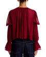 Sheer burgundy blouse with a V-neckline, gathered shoulders, voluminous long sleeves, and ruffled cuffs, tucked into dark-wash jeans against a light gray background.