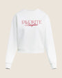 Product image of a white-colored cropped sweatshirt with a crew neckline, long sleeves, and ribbed cuffs and hem. The sweatshirt features the text “FAVORITE Daughter” printed across the chest in red lettering and is shown laid flat against a light neutral background.