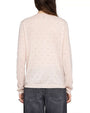 Back view of a person wearing a light pink long-sleeve sweater embellished with small, evenly spaced rhinestones. The sweater has a straight hem and a relaxed fit. It is paired with high-waisted, faded black jeans featuring visible back pockets. The person’s arms are relaxed by the sides, and long straight hair falls down the back.