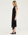 Side view of a black sleeveless midi dress with a draped V-neckline and gathered wrap-effect detailing at the waist. The dress features a slim silhouette and an asymmetrical overlay that extends below the hem. Styled with black pumps and shown against a light gray background.