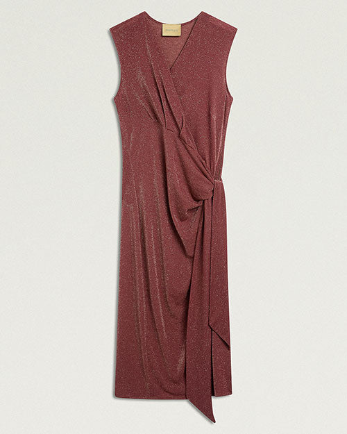 Product image of a sleeveless burgundy midi dress with a subtle metallic shimmer. The dress features a draped V-neckline, wrap-effect construction, and gathered tie detail at the side waist that creates soft pleating through the skirt. An asymmetrical overlay extends from the waist to the hem. Shown laid flat against a light gray background.