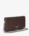 Angled view of a dark brown leather handbag with a silver wing-shaped embellishment on the flap and a silver chain strap placed in front.