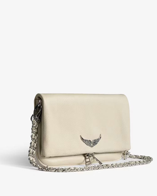 Angled view of an ivory leather clutch bag featuring a silver wing emblem on the front flap, a silver chain strap, and zipper detail, displayed against a light background.