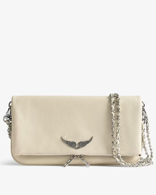 Front view of an ivory leather clutch bag featuring a silver wing emblem on the flap, a silver chain strap, and zipper detail, displayed against a light background.