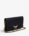 Angled view of a black leather clutch bag featuring a gold wing emblem on the front flap, a gold chain strap, and zipper detail, displayed against a light background.