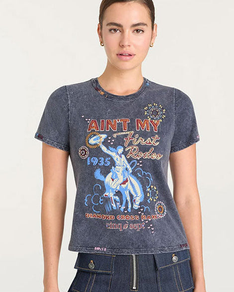Front view of a short-sleeve, faded black graphic T-shirt featuring colorful rodeo-themed artwork. The design includes a cowboy riding a bucking horse in blue tones, surrounded by decorative circular patterns. Text on the shirt reads ‘Ain’t My First Rodeo,’ ‘1935,’ and ‘Diamond Cross Ranch cinq à sept’ in red, yellow, and white lettering.