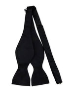 Black self-tie bow tie laid flat, showing its classic shape with wide ends tapering into narrow sections, designed for manual tying.
