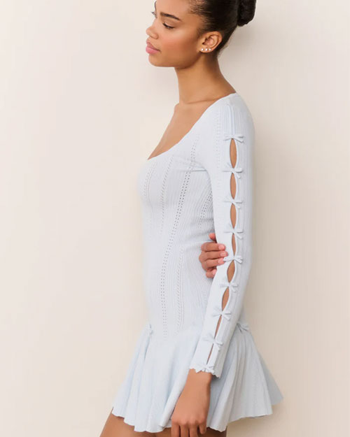 Side view of a light blue long-sleeve knit mini dress with a scoop neckline, fitted bodice, and flared hem. The sleeve features multiple oval cutouts tied with small bows along the arm.