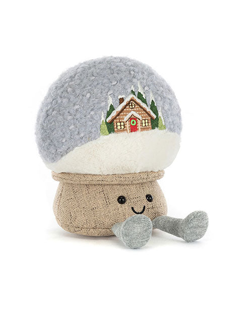 Plush toy shaped like a mushroom with a smiling face, featuring a snow-covered cap embroidered with a house and trees, a burlap-textured stem, and small grey legs and feet.