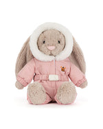 Plush rabbit toy with long floppy ears, dressed in a pink hooded winter outfit with white fur trim, an embroidered orange bell on the chest, matching pink pants, and a white belt.
