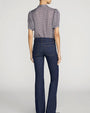 Back view of a small-check print blouse in blue, brown, and cream tones, tucked into dark indigo jeans. The blouse features short puff sleeves with gathered cuffs, a relaxed fit, and gentle gathers at the shoulders and upper back. The jeans have a mid-to-high rise, fitted hips, and a subtle bootcut silhouette with two back patch pockets and contrast stitching. The outfit is shown against a light gray background.