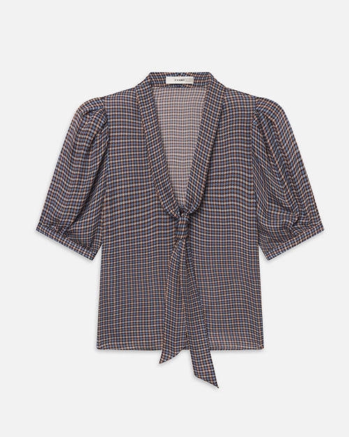 Front view of a short-sleeve blouse featuring a small blue, brown, and cream check pattern. The blouse has a deep V-neckline with a self-tie scarf detail at the front, gathered shoulders, and softly puffed sleeves ending just above the elbows. The lightweight fabric drapes loosely through the body, and the blouse is displayed against a light gray background.