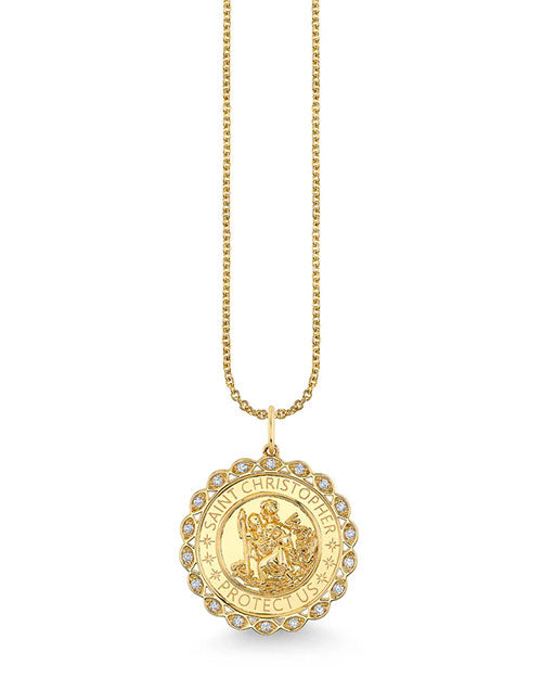 Gold necklace featuring a round Saint Christopher medallion pendant. The pendant has an engraved depiction of Saint Christopher carrying a child, surrounded by the words ‘SAINT CHRISTOPHER PROTECT US.’ The edge of the medallion is scalloped and adorned with small clear gemstones.