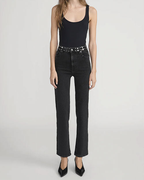 Person wearing a sleeveless black scoop-neck top tucked into high-waisted black jeans with a straight-leg fit, accessorized with a black belt featuring silver studs, and pointed black shoes.