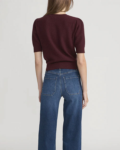 Back view of a short-sleeve textured knit top in deep burgundy paired with high-waisted blue jeans featuring back patch pockets.