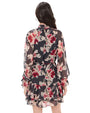 Rear view of a person wearing a black and pink floral chiffon mini dress with a high ruffle neckline, long sheer sleeves with tie cuffs, a cinched waist, and a tiered ruffle hem.