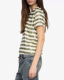 A person is shown from the side wearing a short-sleeve T-shirt with horizontal olive green and white stripes. The shirt has a relaxed fit and a round neckline. The outfit includes high-waisted, faded blue jeans with a straight-leg cut. The person’s left arm is resting naturally by the side.