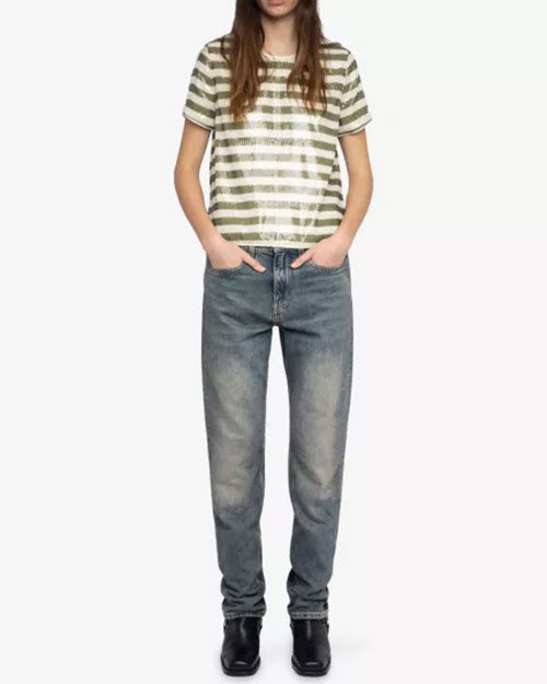  A person is standing against a plain white background wearing a short-sleeve T-shirt with horizontal olive green and white stripes. The shirt has a relaxed fit and a round neckline. The outfit includes high-waisted, straight-leg blue jeans with a faded wash and black shoes. Both hands are placed in the front pockets of the jeans.