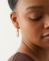 Close-up of an ear wearing a small, gold rectangular link earring with a minimalist design.