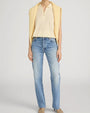 Person standing in a studio against a light neutral background, wearing a soft yellow sleeveless knit polo-style top with a short zipper neckline. A matching yellow sweater is draped over the shoulders. The outfit is paired with mid-rise, straight-leg light-wash jeans and neutral-toned shoes, photographed in a full-length, front-facing pose.