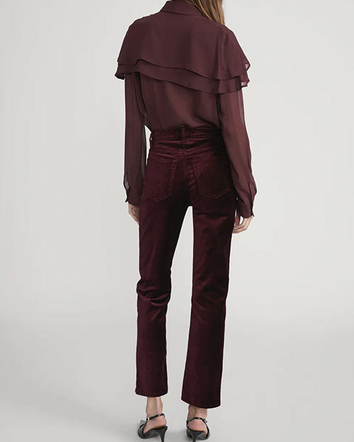 Back view of high-waisted velvet pants in deep burgundy paired with a long-sleeve button-up blouse featuring layered ruffle details.