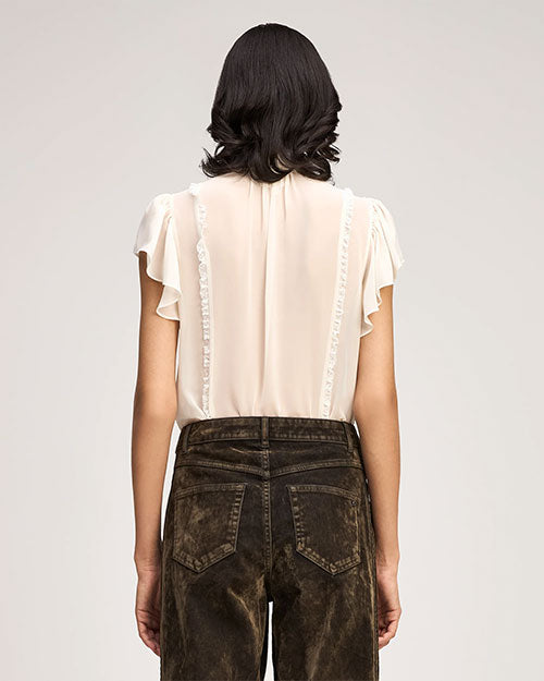 Ivory ruffle-trim blouse with a high neck tie, flutter sleeves, and front button detailing, paired with dark washed jeans.