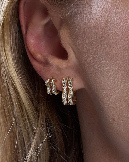 Close-up of an ear wearing two gold earrings, each featuring three parallel rows of small sparkling stones for an elegant design.