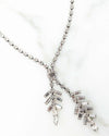 Close-up of a silver-toned necklace with a Y-shaped design, featuring two dangling pendants made of baguette-cut crystals arranged in a branch-like pattern, displayed on a white marble surface.