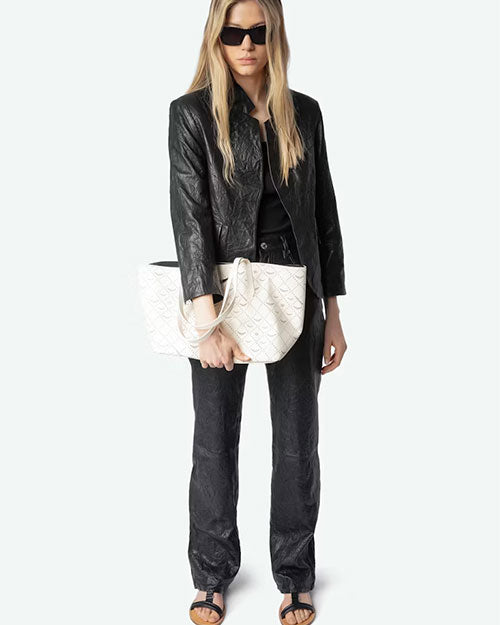 Person wearing a black textured jacket and matching pants, holding a large white tote bag with an embossed pattern. The outfit is paired with black open-toe sandals.
