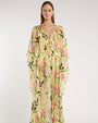 Person standing in a studio against a light neutral background, wearing a sheer, floor-length yellow cover-up with a V-neckline, flowing sleeves, and an adjustable waist tie. The fabric features a floral pattern in shades of pink, green, and lavender. Open-toe heeled sandals are visible, and the image is photographed in a full-length, front-facing pose.
