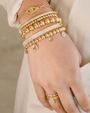 Hand wearing multiple gold beaded bracelets and a ring on a neutral background