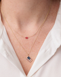 Two gold necklaces with red and blue pendants on a white shirt background