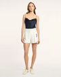 Woman wearing a navy satin top and white shorts with a logo on a white background