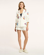 Woman wearing a white embroidered blazer and shorts on a light background