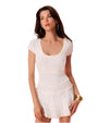 A brunette model wearing large gold hoops and a white dress with thin light blue stripes and a lightly ruffled skirt.