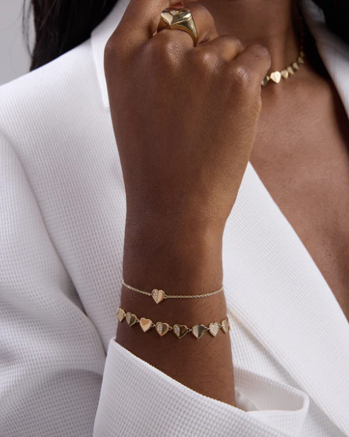 Gold heart-shaped bracelets on a person's wrist against a white background