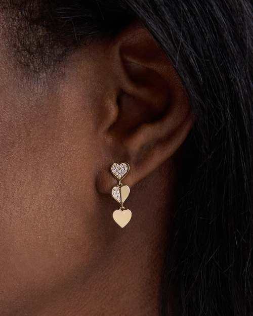 Gold heart-shaped earrings worn by a person with dark hair.