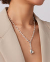 A close-up of a woman’s neck adorned with a silver necklace that has a heart charm, highlighting her style.