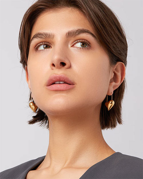A woman adorned with shiny gold hoop heart earrings, highlighting her fashionable and chic appearance.