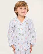Child wearing a white pajama set featuring a long-sleeved, collared button-up shirt and matching pants, both adorned with colorful illustrations of animals, people, and nature scenes, standing against a plain background.